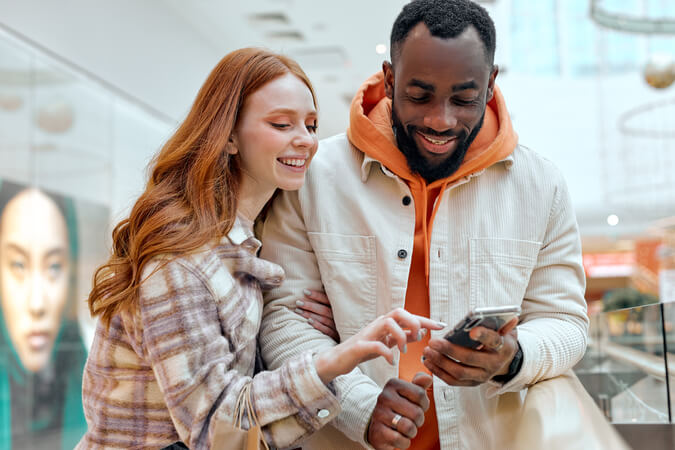 Two people looking at a phone in a mall, representing customers you can reach with consumer marketing lists.