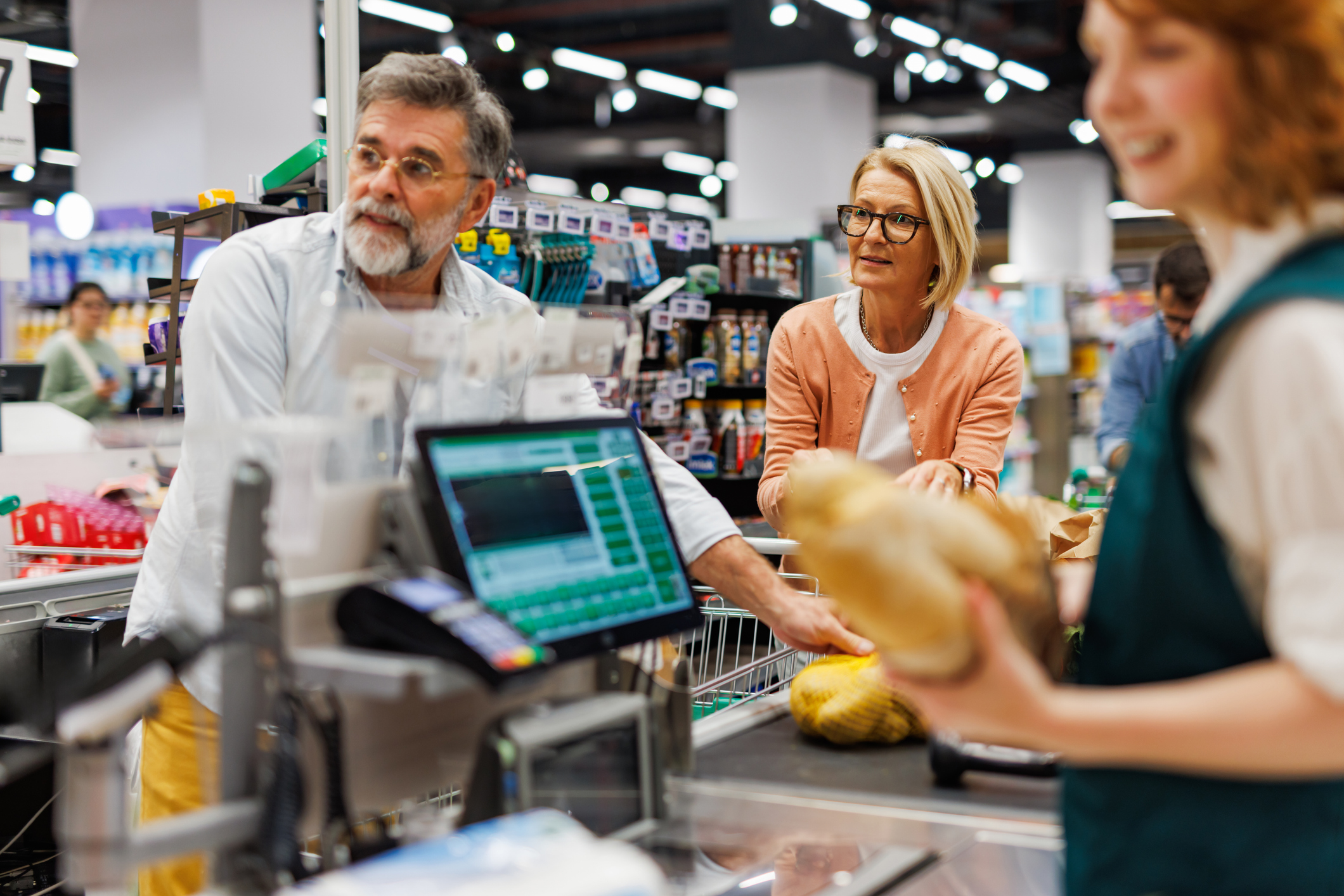 Senior couple buying groceries at checkout counter with cashier scanning items